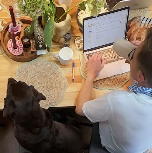 A dog resting its head on the table next to a laptop