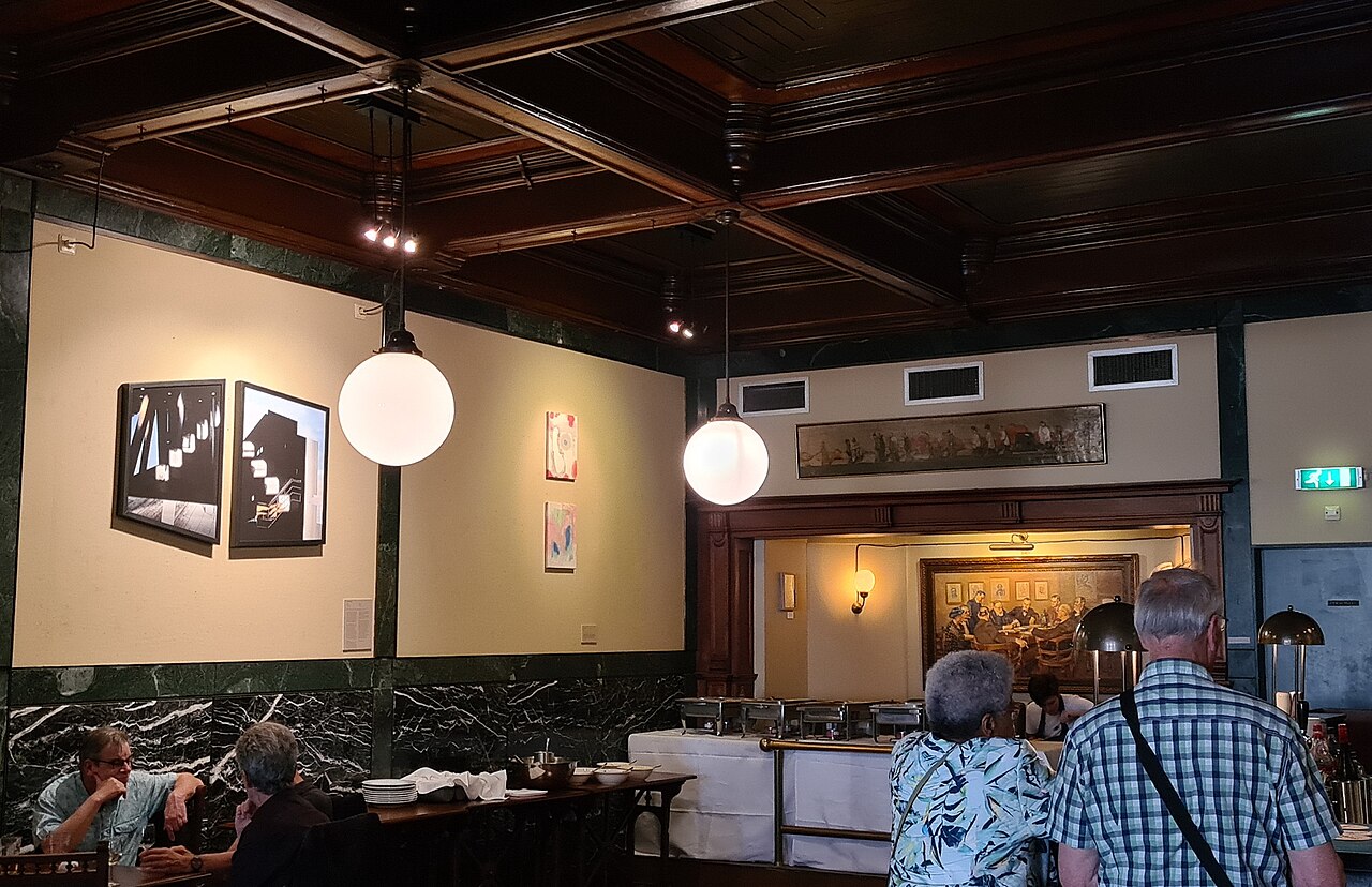 The society room at Arti et Amicitiae: tables under a dark beamed ceiling with globe lamps and paintings on the walls