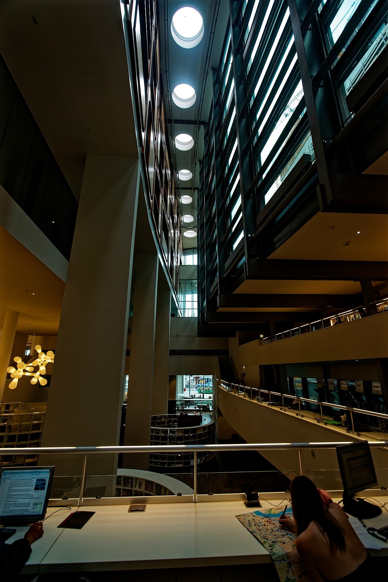People working at a long desk with computer screens along the railing above the library's atrium